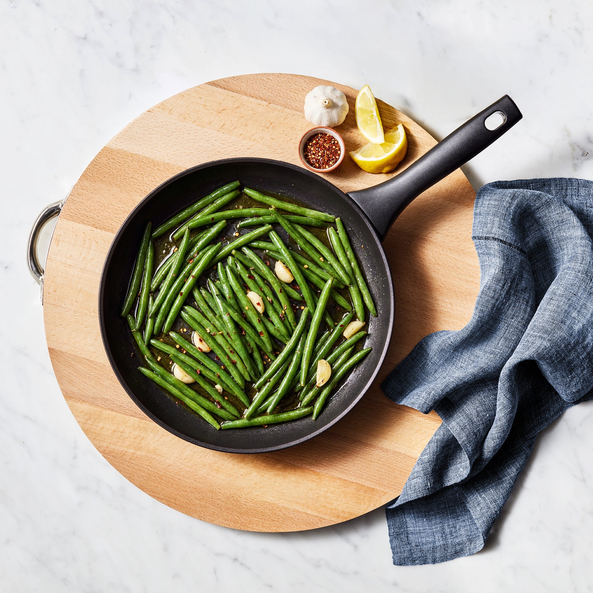 Essteele Per Domani Ceramic skillet with green beans, garlic and ergonomic handle on wooden board.